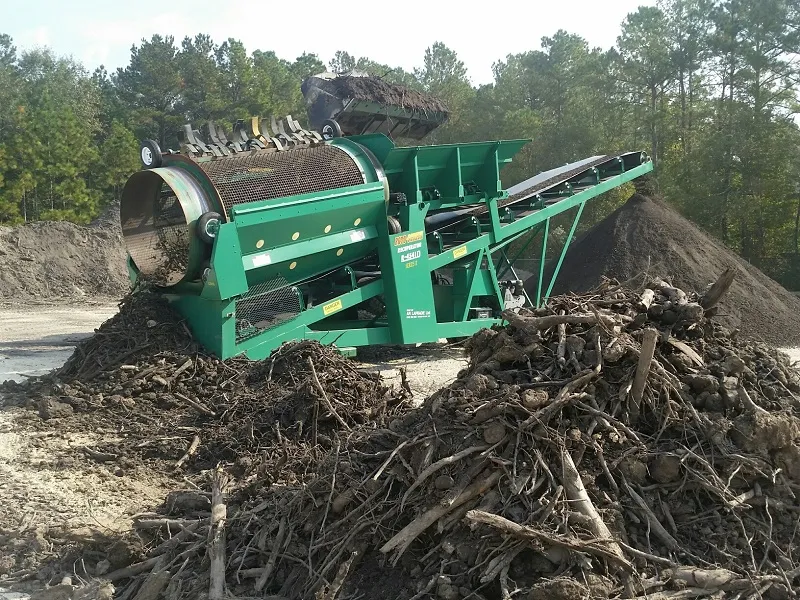 Heavy machinery processing organic material with piles of debris nearby.